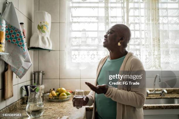 contemplative senior woman taking medicine at home - taking medication stockfoto's en -beelden