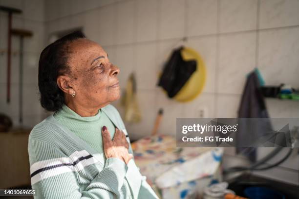 femme âgée contemplative regardant loin à la maison - main sur la poitrine photos et images de collection