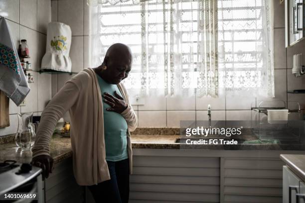 femme âgée ressentant de la douleur à la maison - main sur la poitrine photos et images de collection