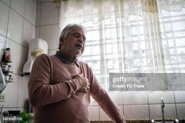 hombre mayor sintiendo dolor en casa - manos sobre el pecho fotografías e imágenes de stock