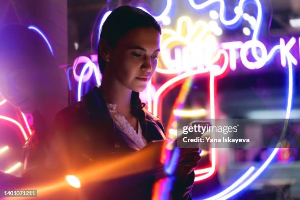 progressive woman is using mobile phone at night in neon lights - fake 個照片及圖片檔