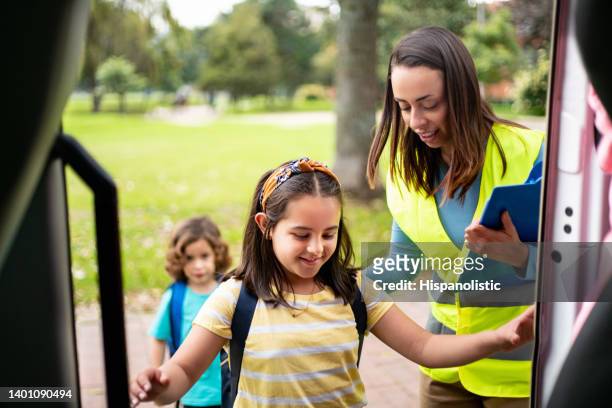 girl boarding the school bus with the help of the bus driver - shuttle bus stock pictures, royalty-free photos & images
