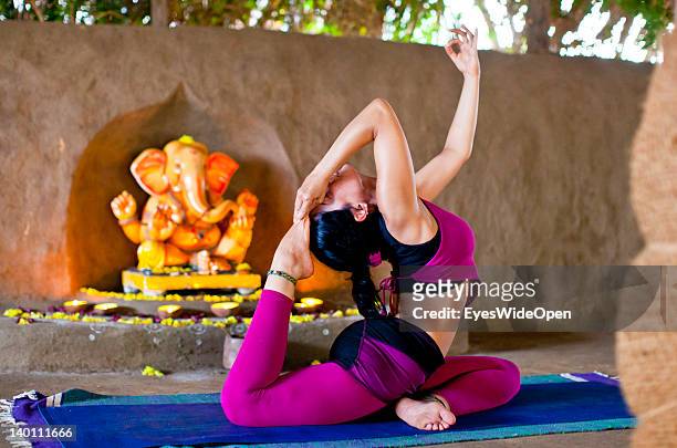 Young women and yoga teacher practices advanced yoga postures and asanas like raja kapotasana, king pigeon pose, in a traditional yoga shala at Yoga...