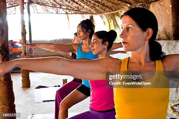 Yoga female tourists practice yoga postures and asanas with a teacher in a class in a traditional yoga shala at Yoga Magic Eco Retreat in Anjuna on...