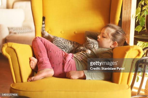 girl sleeping with her cat on chest on yellow armchair - girls cuddling cat stock-fotos und bilder