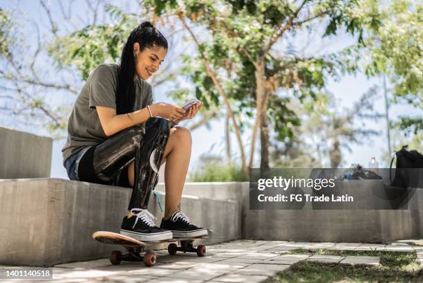 mujer skater discapacitada usando teléfono móvil en el parque - equipo protésico fotografías e imágenes de stock