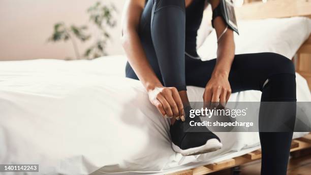 primer plano de una mujer africana preparándose para un entrenamiento en su habitación en casa. una atleta en forma se ata los cordones mientras se prepara para salir a correr - vestirse fotografías e imágenes de stock