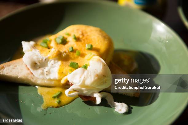 a dish of egg benedict on toast topped with hollandaise sauce - pochiert stock-fotos und bilder