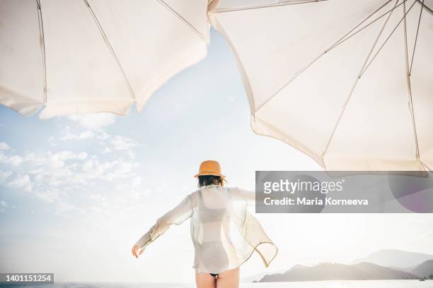 back view of woman walking on beach. - chapeau de soleil photos et images de collection