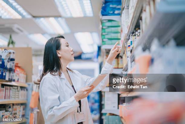 asiatische chinesische apothekerin prüft das inventar im regal in der einzelhandelsapotheke - female pharmacist with a digital tablet stock-fotos und bilder
