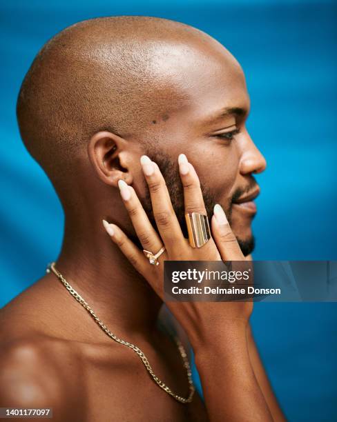 closeup of an african man with a female hand touching his face while standing against a blue background - shaved head profile stock pictures, royalty-free photos & images