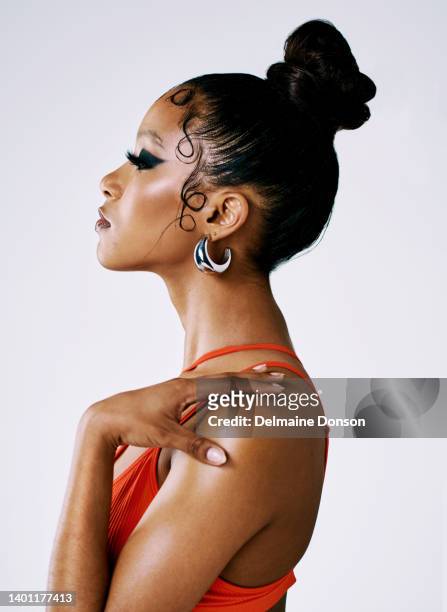 beautiful african woman wearing fashion makeup in a studio against a grey background. side profile of a woman looking away wearing a red swimsuit and smokey black eyeshadow. beauty and glamour - female model hair bun stock pictures, royalty-free photos & images
