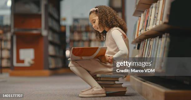 niña sentada en libros en la biblioteca y leyendo un libro. linda chica con el pelo rizado haciendo su proyecto. mujer sola y haciendo investigación para un proyecto - literature fotografías e imágenes de stock