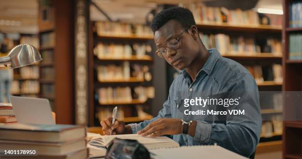 uomo africano seduto all'interno di una biblioteca da solo a fare ricerche. uomo che lavora su un progetto. giovane che fa ricerche per un caso. avvocato che lavora su un caso - research foto e immagini stock