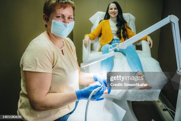 portrait of pedicurist using an electric tool while doing a pedicure on feet of woman - sjukvårdsrelaterat material bildbanksfoton och bilder