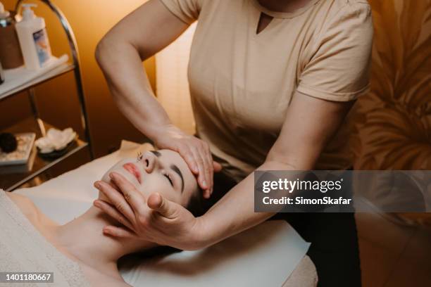 massage therapist performing head massage on young woman - head massage stock pictures, royalty-free photos & images