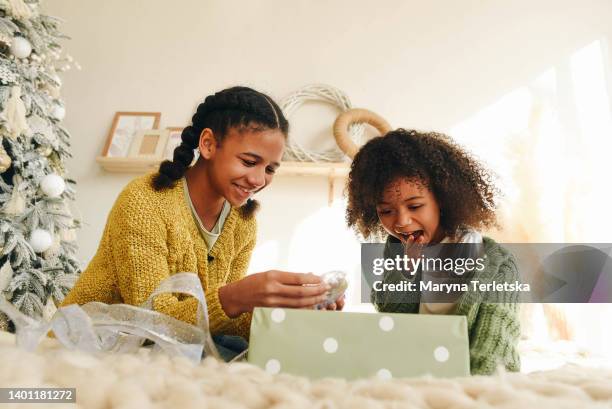 two afro sisters sit on a large bed and open a gift. room design in light colors. christmas mood. christmas presents. - open day 5 stock pictures, royalty-free photos & images