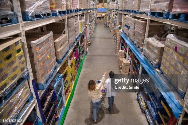 couple pushing trolley down aisle of massive wholesaler - supermarket trolley female stock-fotos und bilder