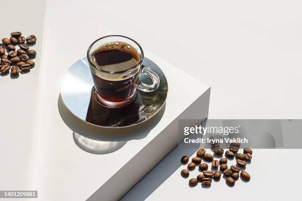 aromatic morning coffee in glass cup and a long shadow from the cup on beige  color background. - coffee crop foto e immagini stock