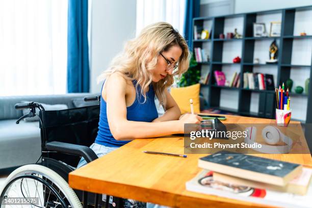 mujer de negocios discapacitada sentada en silla de ruedas trabajando con tableta digital en el lugar de trabajo - arab businesswoman with books fotografías e imágenes de stock