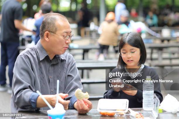 child with smartphone while resting and eating lunch with her father. original phone cover created by herself - filipino family eating stock pictures, royalty-free photos & images