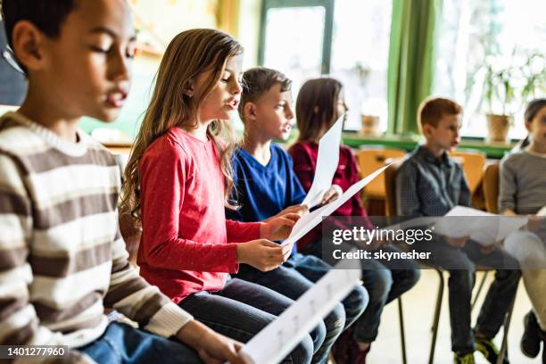 school kids practicing with sheet music on a class at school. - kids singing stock pictures, royalty-free photos & images