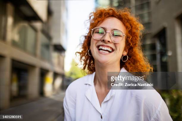une femme d’affaires souriante se tient devant un immeuble de bureaux - cats eye glasses photos et images de collection