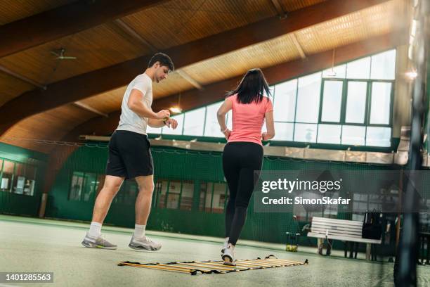 mujeres jóvenes que practican salto de escalera de cuerda bajo la guía de un instructor masculino en la cancha de tenis - entrenamiento deportivo fotografías e imágenes de stock