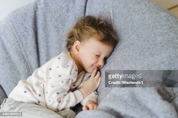 smiling girl lying down on bean bag at home - chupando dedo - fotografias e filmes do acervo