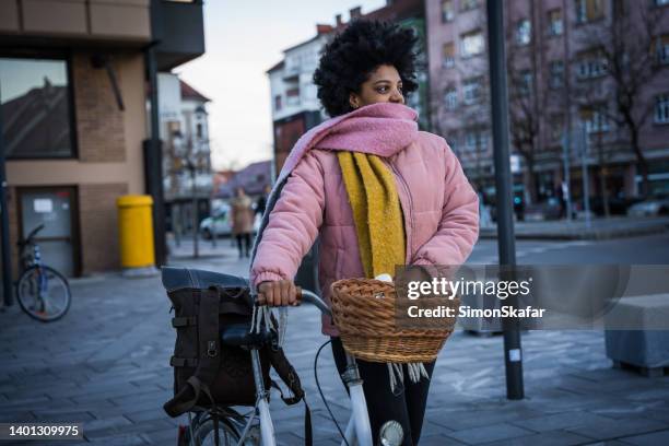 une jeune femme marchant avec son vélo sur le trottoir en ville - panier de bicyclette photos et images de collection