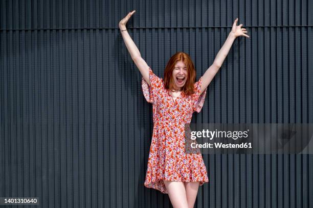 young woman standing in front of wall screaming with arms raised - floral pattern dress stock-fotos und bilder