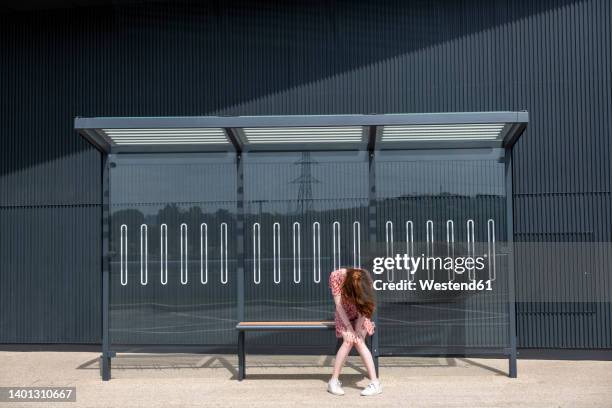 sad young woman sitting alone at bus stop - metal-bench stock pictures, royalty-free photos & images