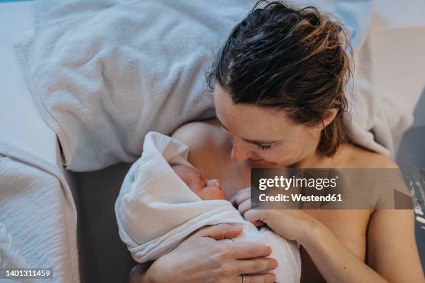 mother holding baby wrapped in towel at home - home birth stock-fotos und bilder
