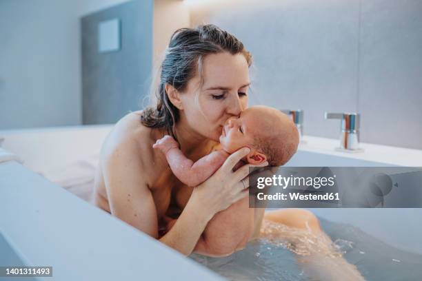 woman kissing baby boy in bathtub at home - home birth stock-fotos und bilder