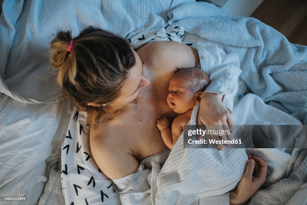 Baby sleeping on mother's chest in bed at home
