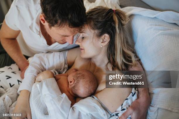 father embracing woman and son lying on bed at home - childbirth stock pictures, royalty-free photos & images