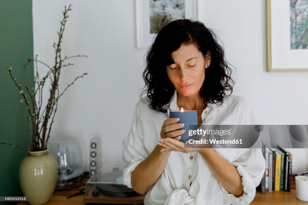 Woman with eyes closed holding candle in living room at home