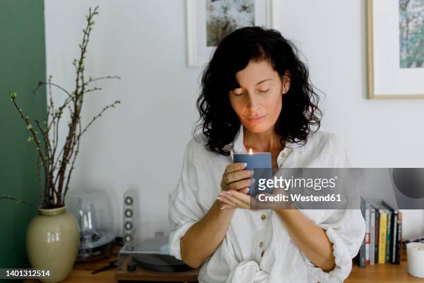 woman with eyes closed holding candle in living room at home - scented 個照片及圖片檔