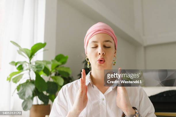 woman with eyes closed doing breathing exercise in living room at home - inhaling stockfoto's en -beelden