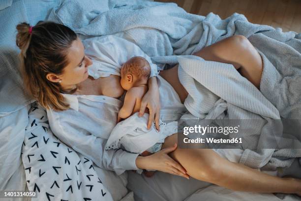 mother lying on bed breastfeeding baby at home - home birth stock-fotos und bilder