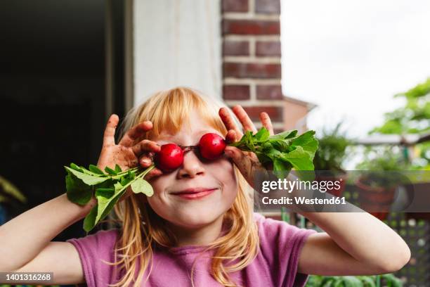 smiling girl covering eyes with fresh radish on balcony - radijs stockfoto's en -beelden