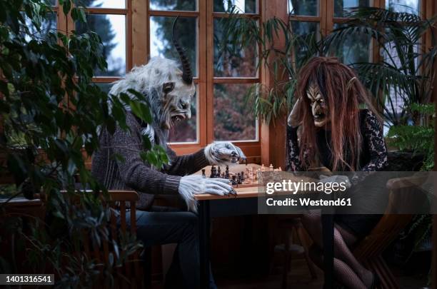 man and woman in spooky costumes playing chess sitting at table - krampus stock pictures, royalty-free photos & images