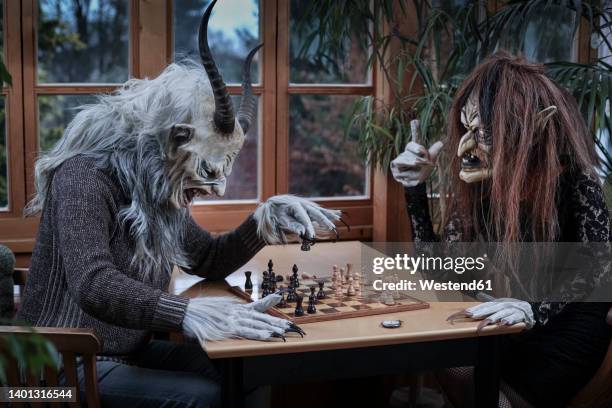 mature man and woman in ghost costume playing chess game sitting at table - krampus stock pictures, royalty-free photos & images