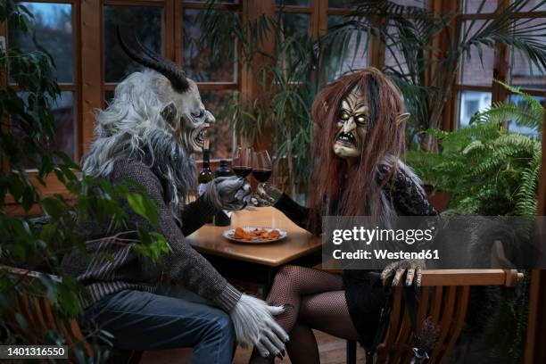 man and woman in spooky costume toasting wine glasses sitting at table - krampus stock pictures, royalty-free photos & images