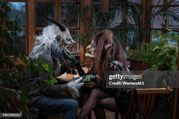 krampus and witch with wineglass holding hands sitting at table - krampus stock pictures, royalty-free photos & images