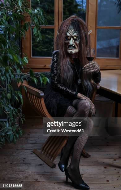 woman wearing witch costume sitting with wineglass on chair at horror house - krampus stock pictures, royalty-free photos & images