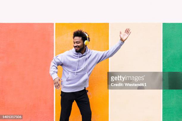 happy man listening music through headphones and dancing in front of colorful wall - man and his hoodie imagens e fotografias de stock