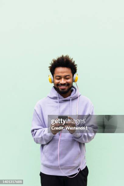 smiling man using mobile phone and listening music through headphones against turquoise background - headphones isolated foto e immagini stock