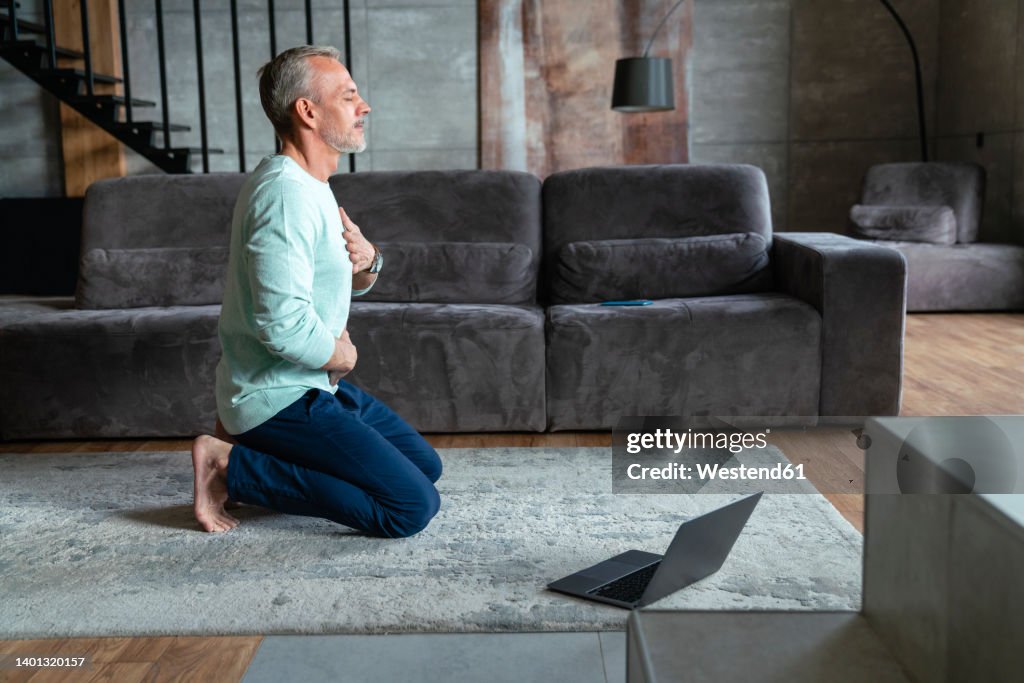 Man with eyes closed exercising on carpet in living room at home