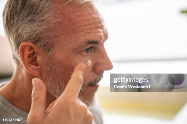 man applying cream on face in bathroom - hombre crema facial fotografías e imágenes de stock